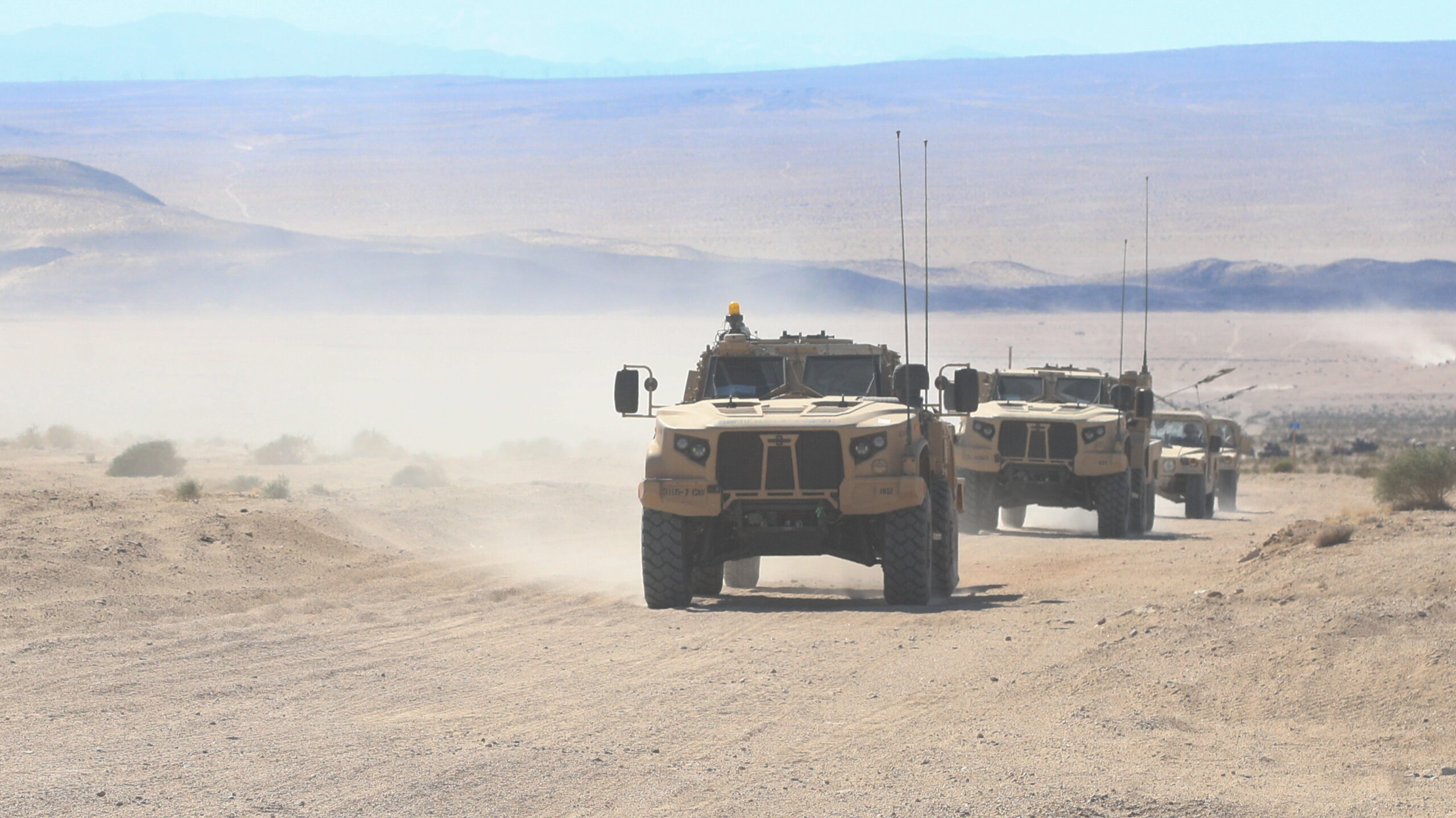 Line of JLTVs driving through a desert landscape